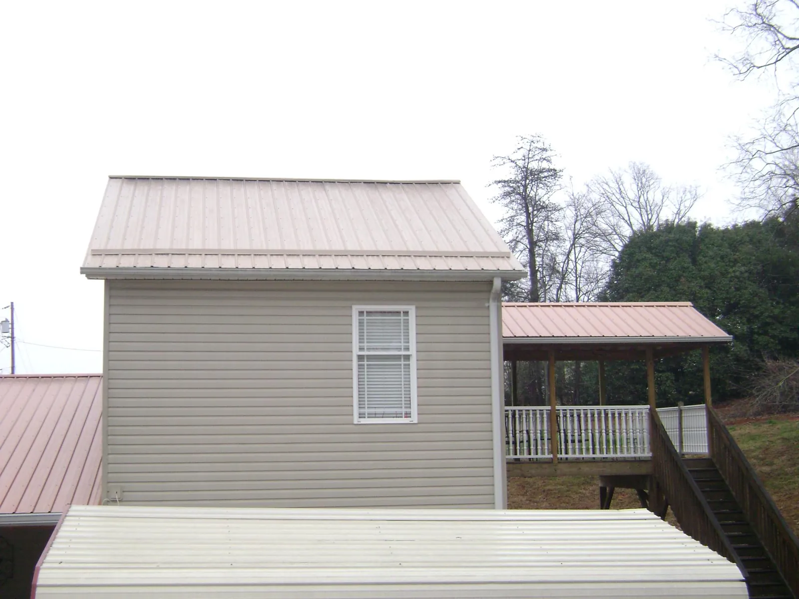 Tan metal roofs on a two story addition and attached porch, from a Roof Replacement job in Sharon